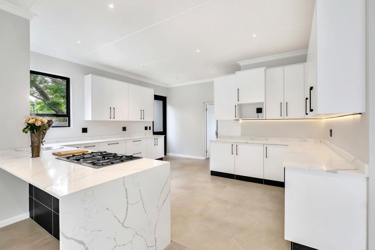 Modern, bright kitchen featuring white cabinetry, marble-look stone countertops, a central island with a gas hob, and sleek under-cabinet lighting.
