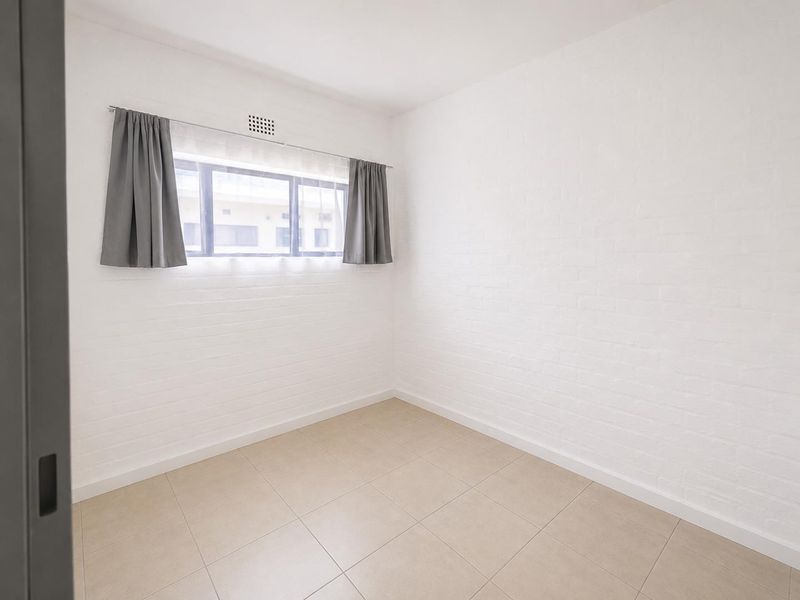 A bright, empty bedroom featuring neutral tiled flooring and clean white painted brick walls, ready for personalization.