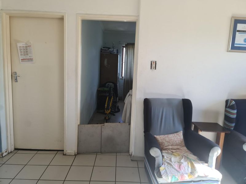 A hallway area featuring tiled flooring and a doorway with a makeshift barrier, showing signs of wear and maintenance requirements.