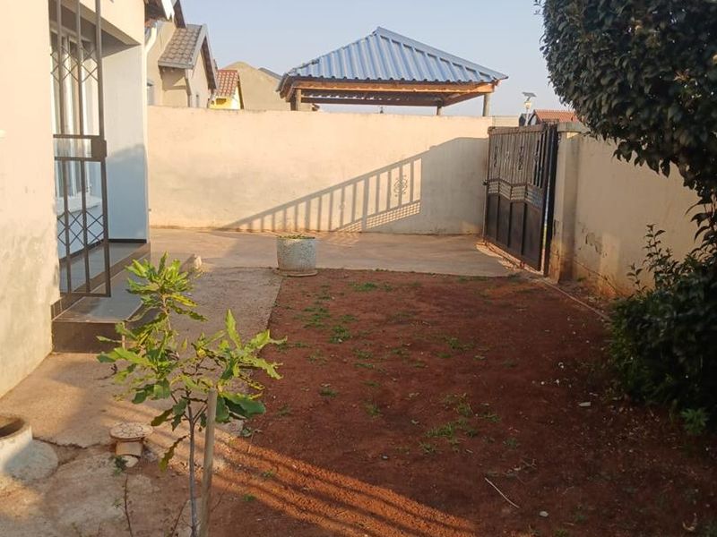 Rear garden area featuring a concrete paved section, perimeter wall with security gate, and a detached gazebo structure.