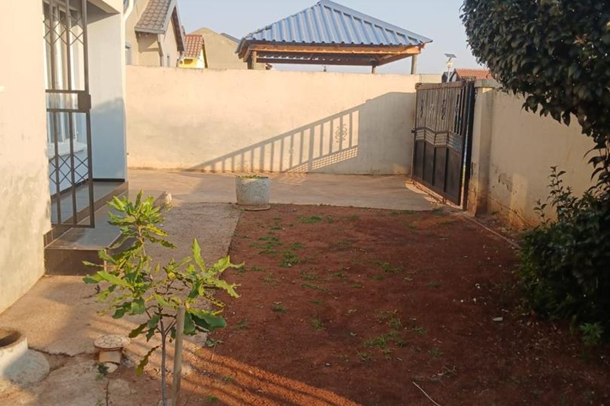 Rear garden area featuring a concrete paved section, perimeter wall with security gate, and a detached gazebo structure.