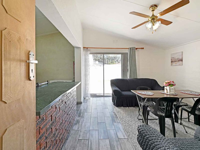 Open-plan living and dining area featuring a brick breakfast bar, vaulted ceilings, ceiling fan, and sliding glass door access to the exterior.