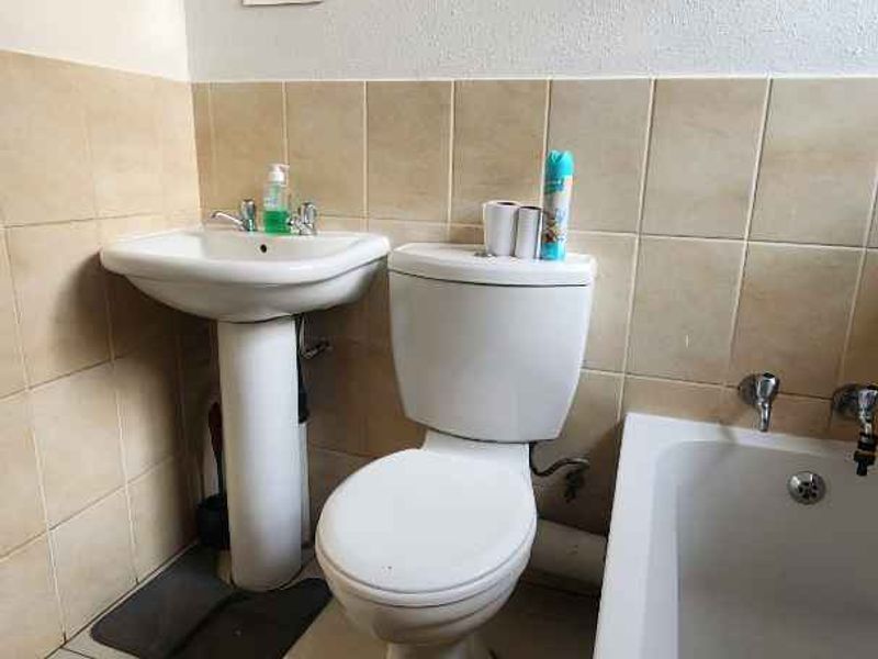 A functional bathroom featuring a pedestal basin, standard toilet, and bathtub with tiled splashbacks and neutral floor tiles.