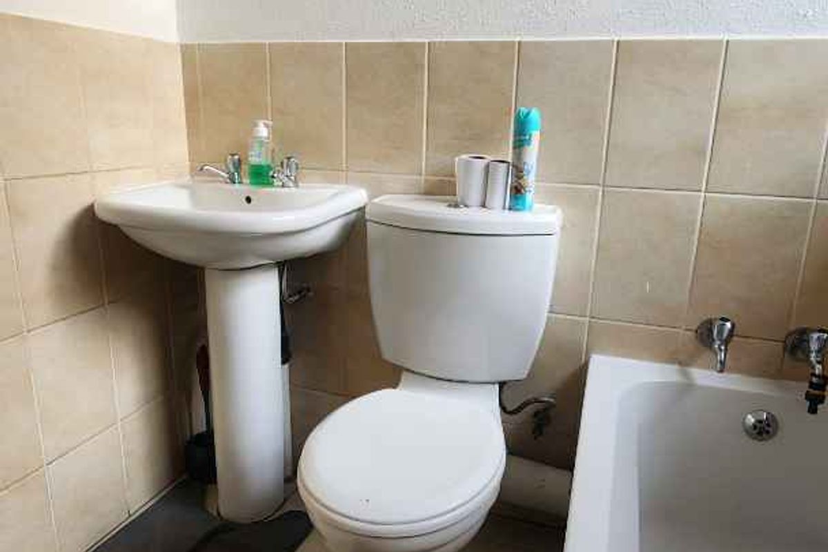 A functional bathroom featuring a pedestal basin, standard toilet, and bathtub with tiled splashbacks and neutral floor tiles.