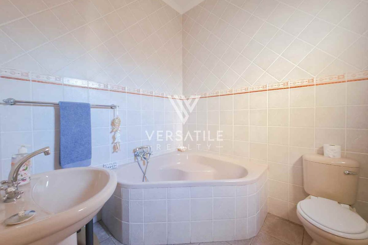A functional bathroom featuring a corner bathtub, pedestal sink, and toilet with neutral wall tiling and decorative border accents.