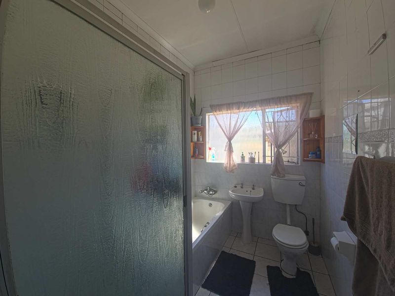 A dated bathroom featuring a bathtub, pedestal sink, toilet, and full-height wall tiling, requiring modernization to improve its aesthetic and functional appeal.
