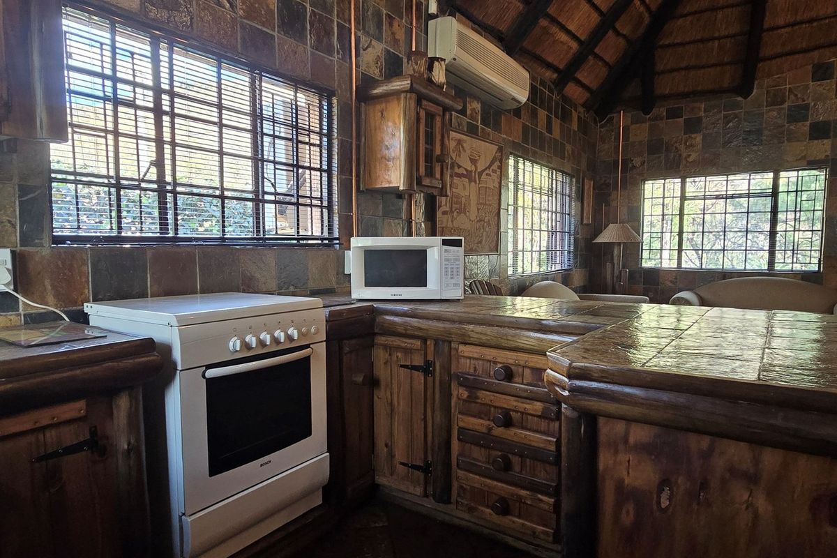 Rustic kitchen featuring stone wall cladding, a thatch ceiling, built-in wooden cabinetry, and a tiled countertop with a freestanding stove.