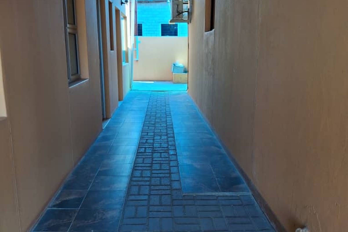 A covered side walkway featuring tiled flooring, a corrugated metal roof structure, and exterior wall-mounted lighting.