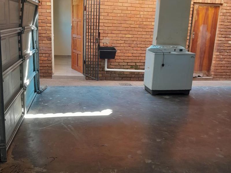 A functional garage space featuring exposed brick walls, concrete flooring, a utility sink, and direct access to the home's interior.