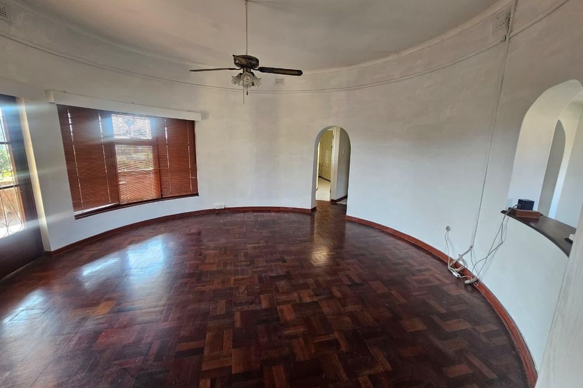A spacious, circular living room featuring original parquet flooring, a ceiling fan, and an arched entryway, offering a unique architectural layout.