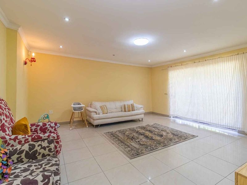 Spacious living room featuring neutral tiled flooring, recessed downlighting, and large sliding glass doors with vertical blinds providing ample natural light.
