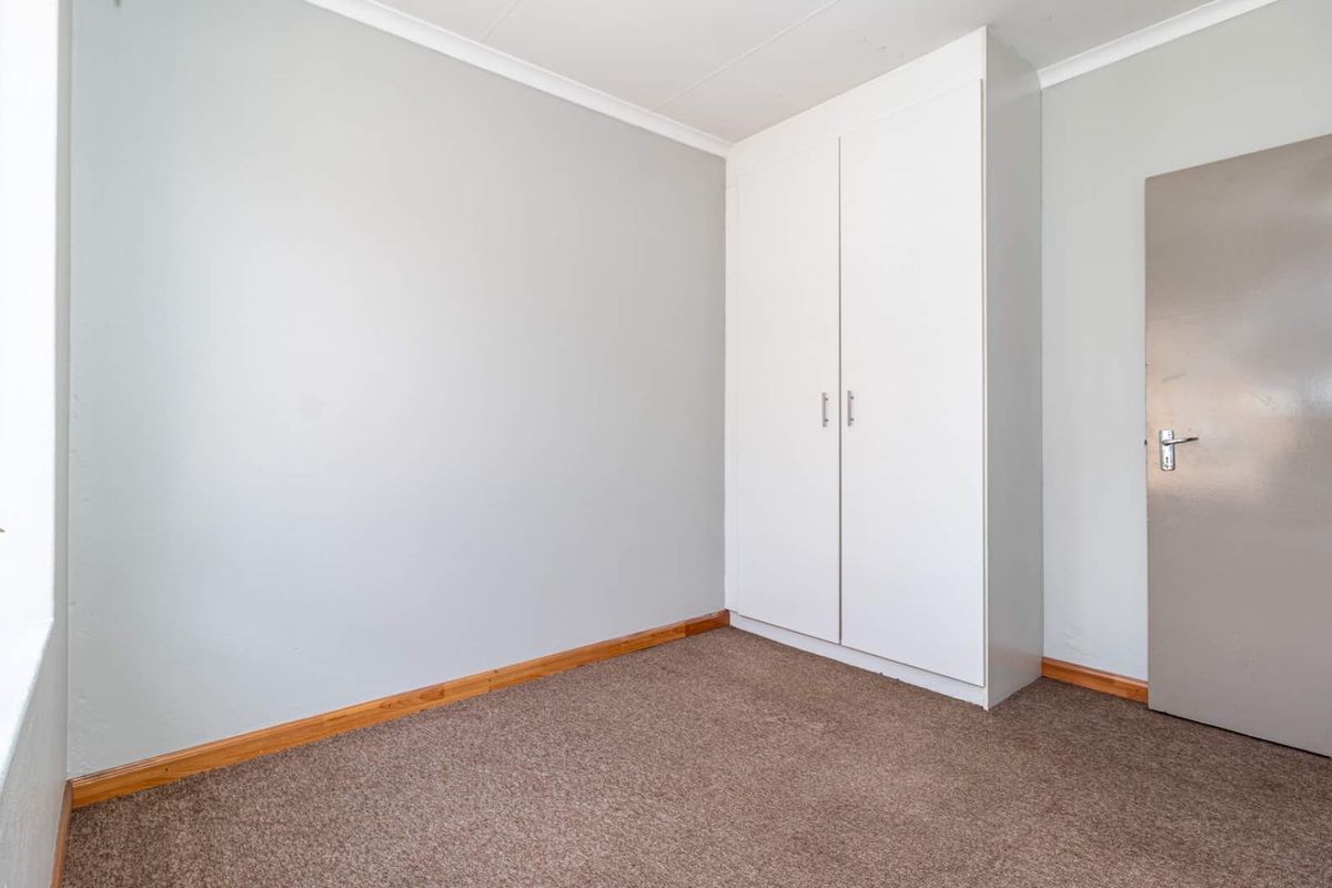A clean, neutral bedroom featuring built-in cupboards and carpeted flooring, offering a blank canvas for personalization.