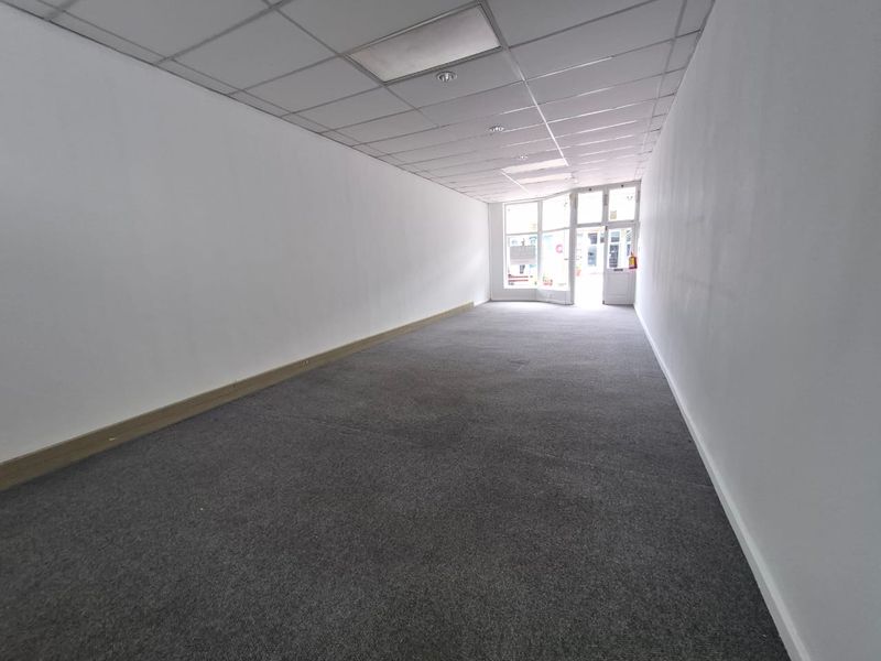 A vacant, open-plan retail space featuring a suspended ceiling, recessed lighting, and large storefront windows providing natural light and street visibility.