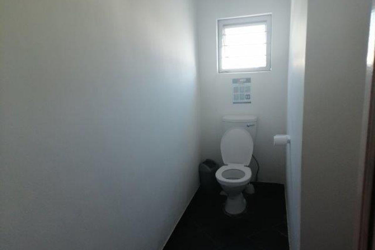 A functional office restroom featuring a standard toilet, tiled flooring, and a small window for natural ventilation.