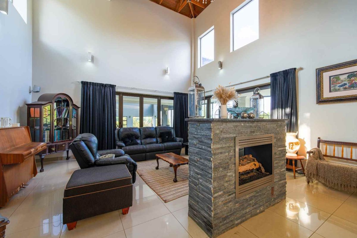 Spacious living room featuring a double-volume ceiling, tiled flooring, and a central stone-clad fireplace partition.