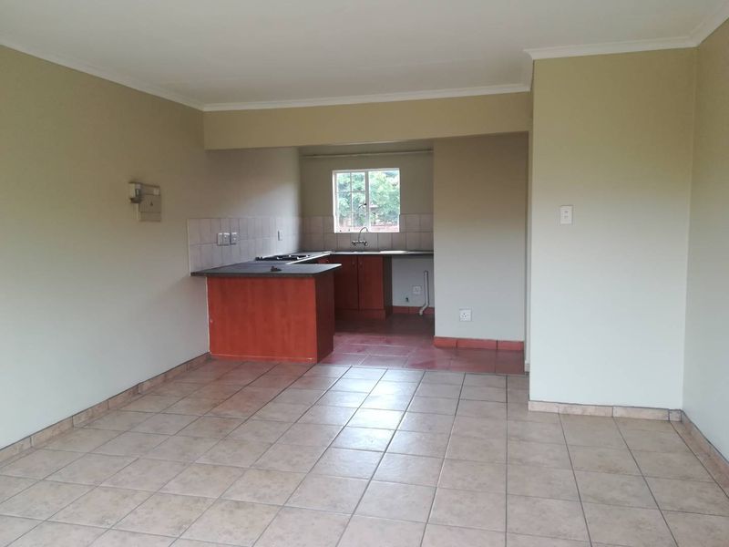 An open-plan living and kitchen area featuring tiled flooring, built-in kitchen cabinetry with a hob, and a neutral color palette.