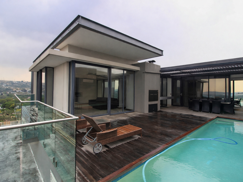 Spacious penthouse terrace featuring a private swimming pool, timber decking, glass balustrades, and seamless indoor-outdoor flow through large sliding doors.