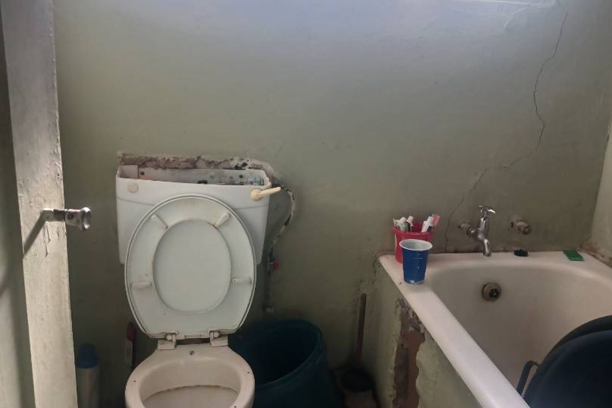 A dated bathroom featuring a bathtub and toilet, currently requiring significant renovation and repair to the wall finishes and overall infrastructure.