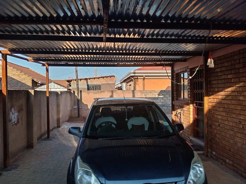A covered carport area featuring a corrugated metal roof, brick wall construction, and paved driveway, providing sheltered off-street parking.