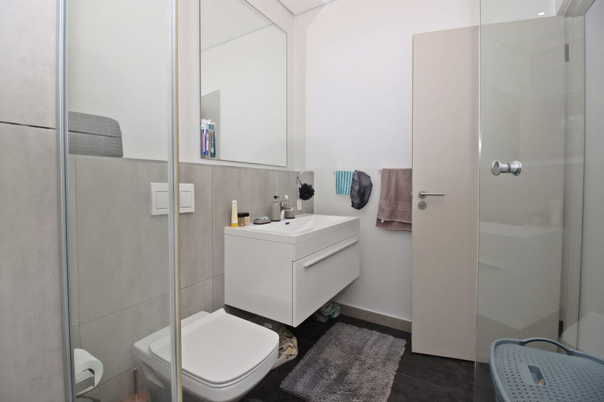 Modern bathroom featuring a wall-mounted vanity with integrated basin, large mirror, and a glass-enclosed shower with contemporary grey tiling.