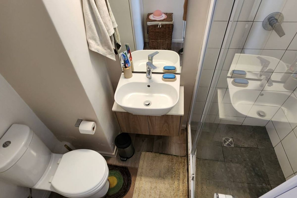 Compact bathroom featuring a modern vanity with basin, a wall-mounted toilet, and a glass-enclosed shower with tiled walls.