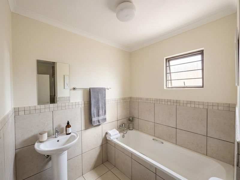 A functional bathroom featuring a pedestal basin, a standard bathtub with tiled surround, and neutral wall finishes.