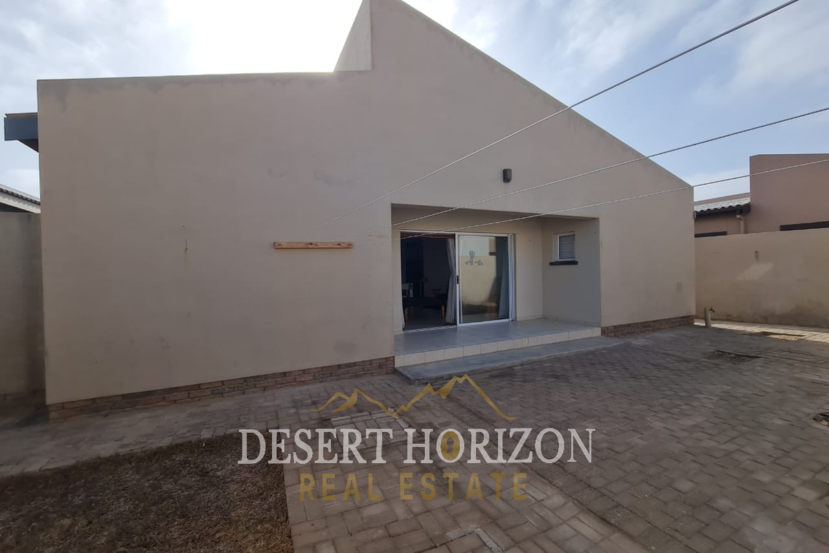 Rear view of the property featuring a paved courtyard, covered patio area, and sliding glass door access.