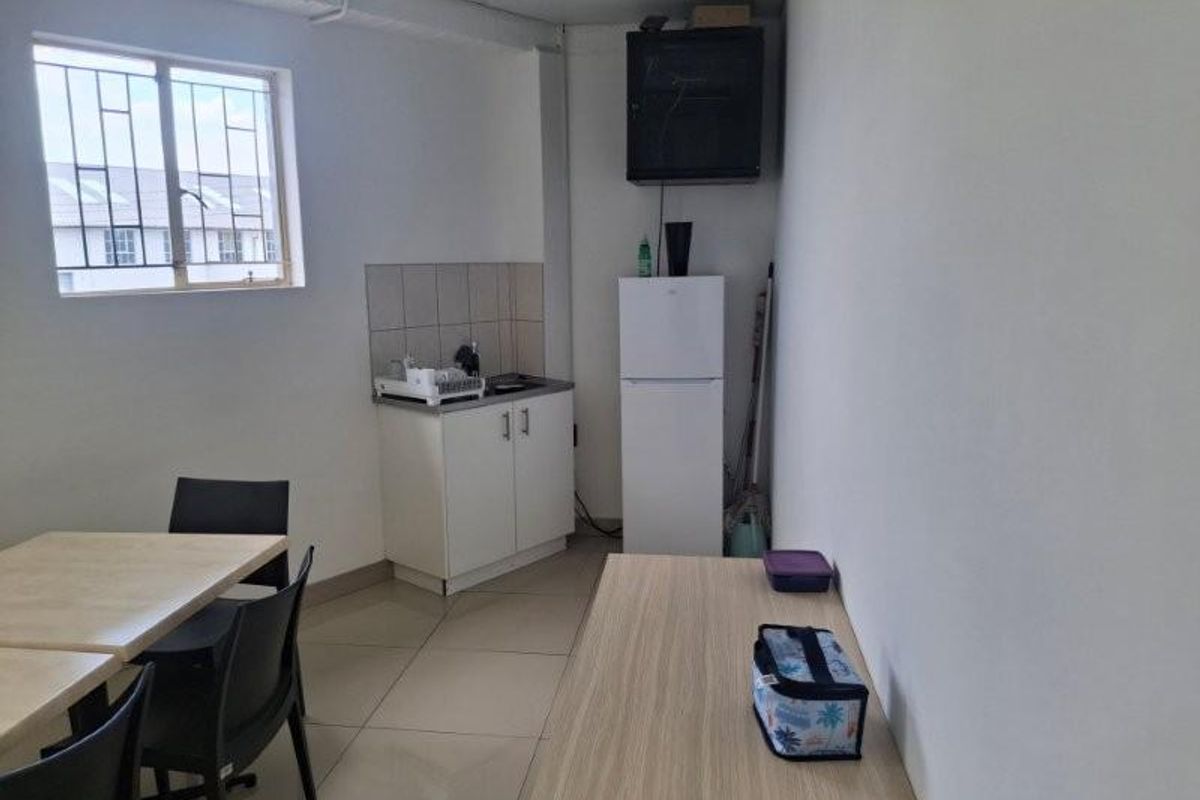 A compact office kitchenette featuring a small sink, base cabinetry, tiled splashback, and a window with security bars.