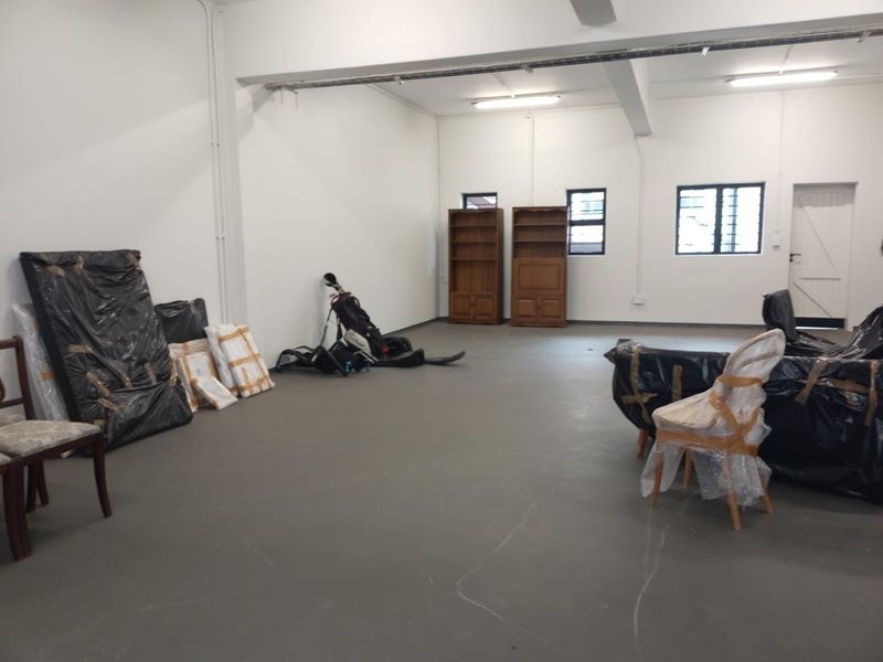 A spacious, open-plan industrial utility area featuring concrete flooring, exposed electrical conduits, and functional windows with security bars.