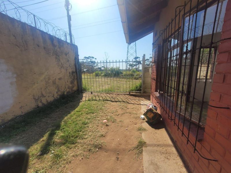 Rear exterior area of the cottage featuring a brick facade, security bars on windows, and a perimeter wall with razor wire.