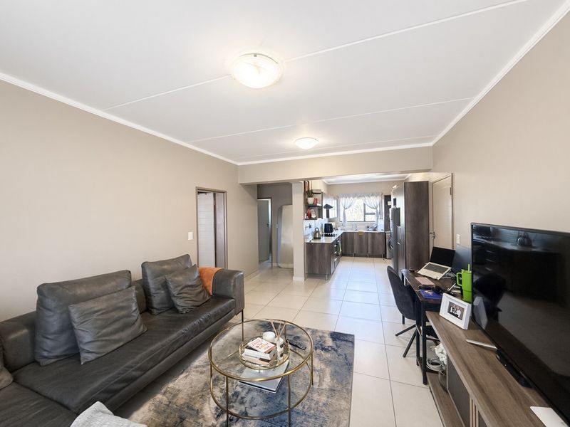 An open-plan living area featuring tiled flooring, neutral walls, and a functional kitchen with modern cabinetry and built-in appliances.