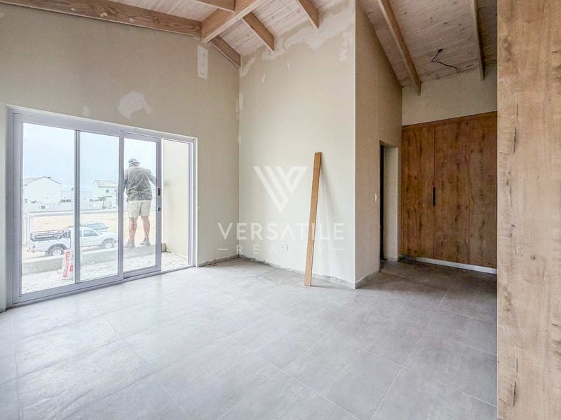 An unfinished bedroom featuring exposed timber ceiling beams, tiled flooring, built-in cupboards, and a sliding glass door leading to the exterior.