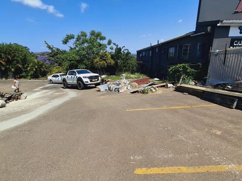 Exterior view of a commercial property featuring an asphalt parking area and building facade, currently showing significant site debris.