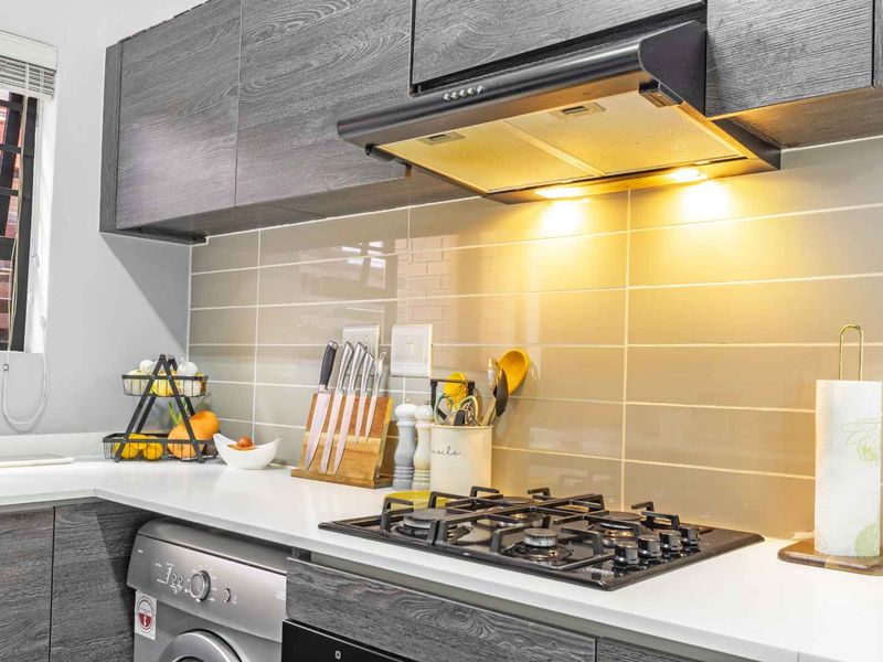 Modern kitchen featuring dark wood-grain cabinetry, stone countertops, a gas hob with extractor fan, and a sleek subway tile backsplash.