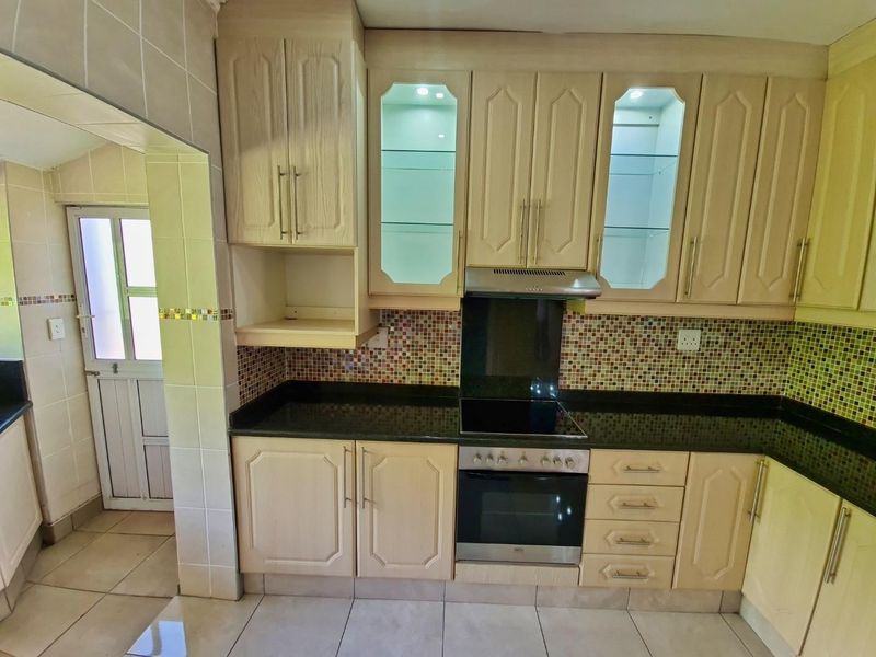 A functional kitchen featuring light wood cabinetry, granite countertops, a mosaic tile backsplash, and integrated appliances including an oven and hob.