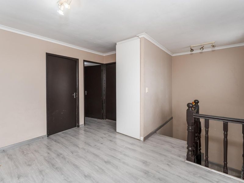 A spacious upper-level hallway featuring light-toned laminate flooring, a traditional wooden staircase railing, and neutral wall finishes.