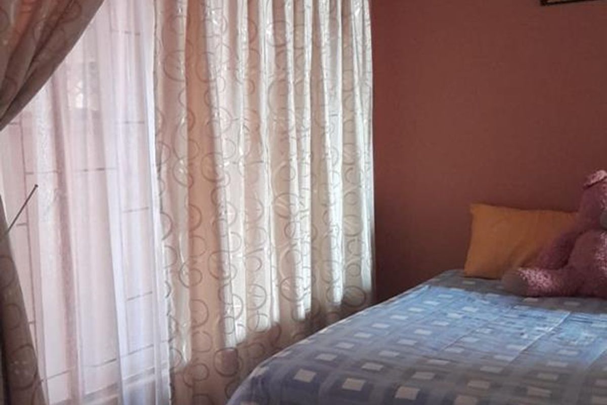 A bedroom featuring tiled flooring and large windows dressed with curtains, providing natural light to the space.