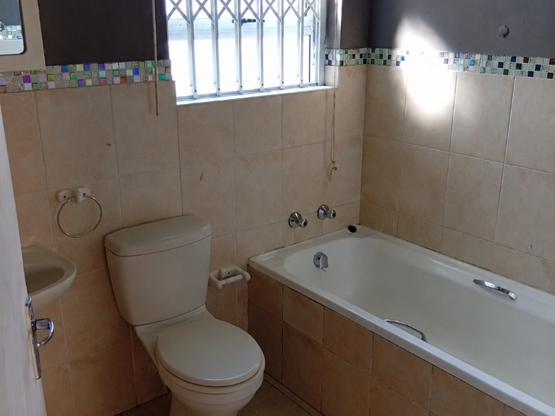 A functional bathroom featuring a bathtub, toilet, and wall-mounted basin, finished with tiled walls and a decorative mosaic border.