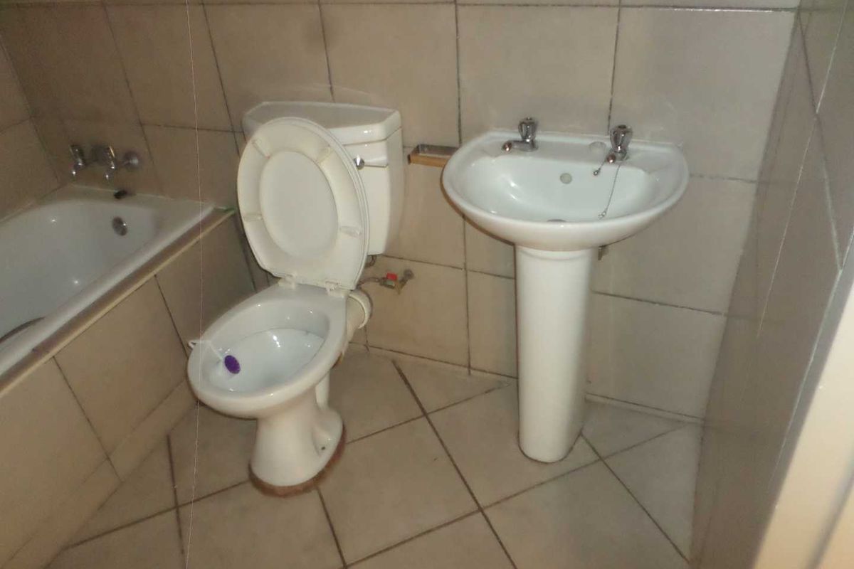 A dated bathroom featuring a standard pedestal basin, toilet, and bathtub with full-height ceramic wall tiling and tiled flooring.