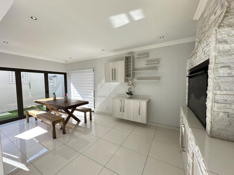 Bright living area featuring a stone-clad built-in fireplace, sleek tiled flooring, and modern built-in cabinetry, with direct access to the outdoor patio.