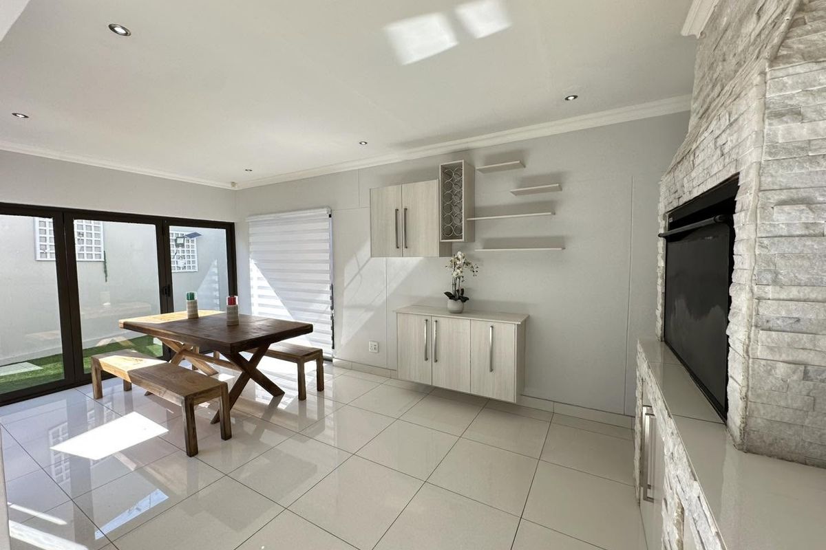 Bright living area featuring a stone-clad built-in fireplace, sleek tiled flooring, and modern built-in cabinetry, with direct access to the outdoor patio.