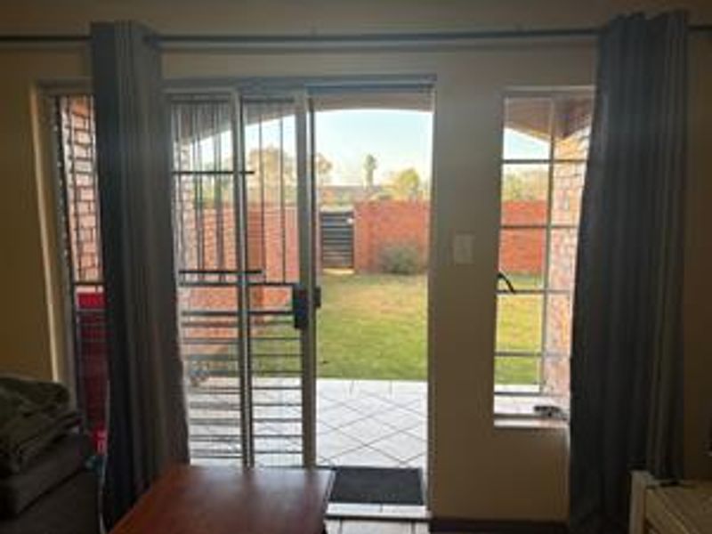 Living room area featuring a sliding glass door with security gate, providing direct access to a tiled patio and private garden.