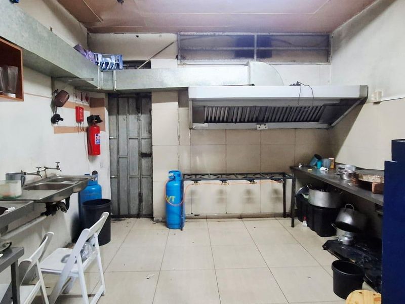 Commercial kitchen space featuring stainless steel sinks, a large extractor hood, tiled surfaces, and gas infrastructure for professional food preparation.