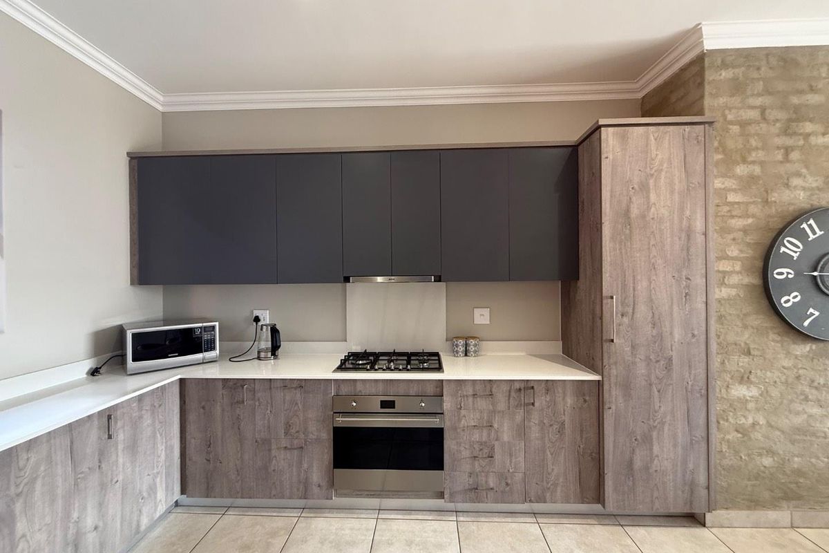 Modern kitchen featuring two-tone cabinetry, stone countertops, built-in oven, gas hob, and extractor fan, complemented by tiled flooring and a feature brick wall.