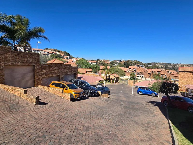 Exterior view of a townhouse complex featuring a paved driveway, brick facade garages, and covered parking areas within a residential estate.