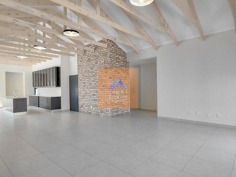 Spacious open-plan living area featuring exposed timber roof trusses, a striking brick feature wall, and a modern kitchen with a central island.