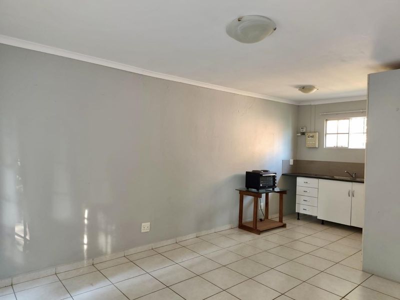 An open-plan living and kitchen area featuring tiled flooring, neutral walls, and basic kitchen cabinetry with a sink.