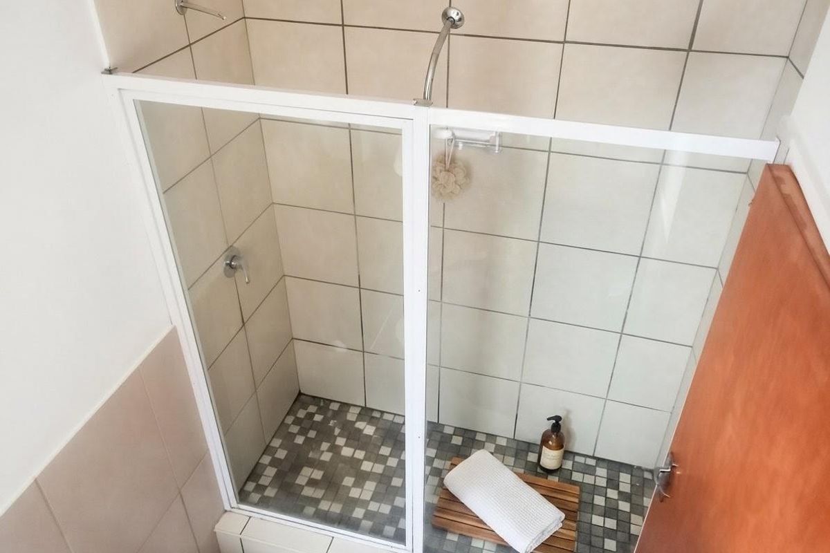 A functional shower stall featuring a white-framed glass enclosure, tiled walls, and a mosaic-tiled floor.