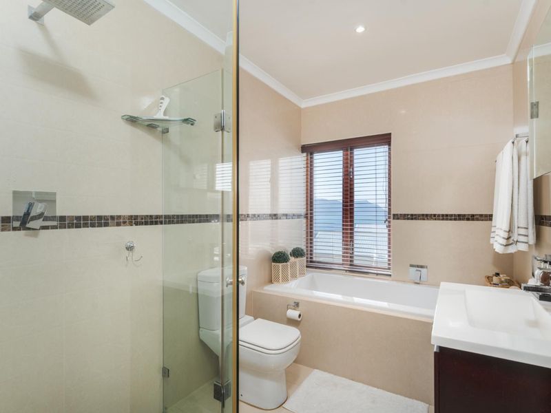 Modern bathroom featuring a glass-enclosed shower, built-in bathtub, vanity basin, and neutral tiled finishes with a window view.
