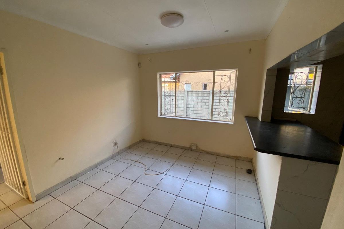An empty living area featuring tiled flooring and a breakfast bar, with security bars on the windows and a security gate at the entrance.